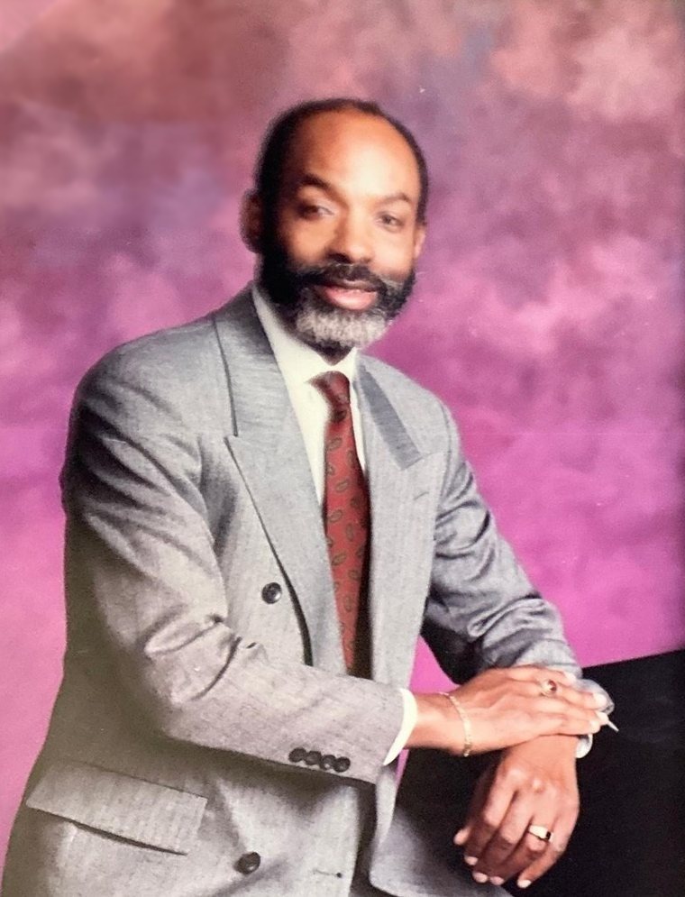 Portrait of Leon Collier in a grey suit and patterned red tie.