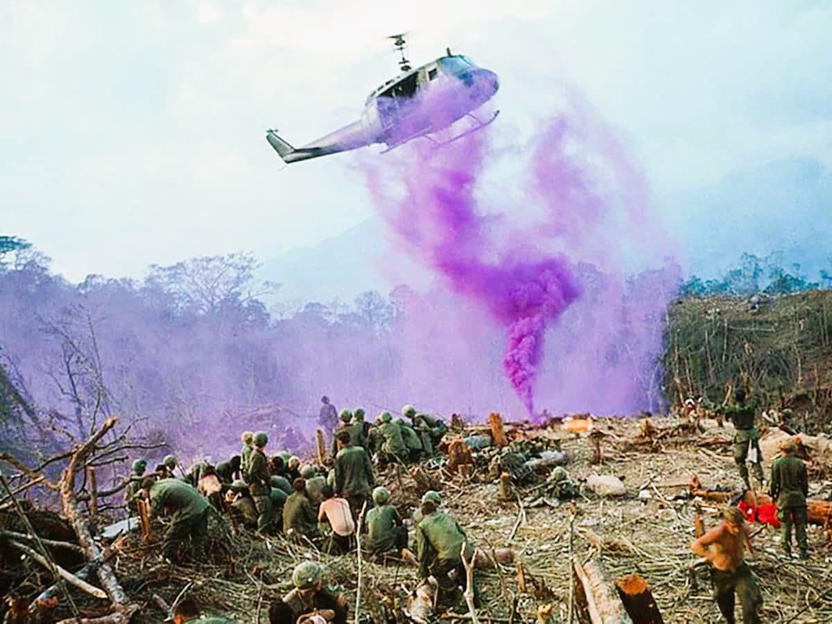 A helicopter above soldiers and colored signal smoke.
